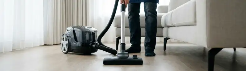 Professional house cleaner vacuuming a living room floor with a canister vacuum cleaner, Milwaukee, WI.