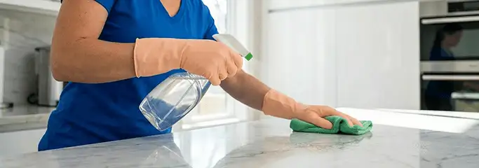 Maid service worker spraying and wiping a kitchen countertop with a microfiber cloth for sanitizing, Milwaukee, WI.