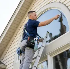 Professional window cleaner on a ladder using a squeegee to clean an exterior arched window, Milwaukee, WI.