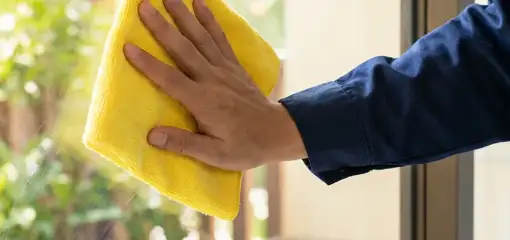 House cleaner wiping a glass window with a yellow microfiber cloth for streak-free cleaning, Milwaukee, WI.